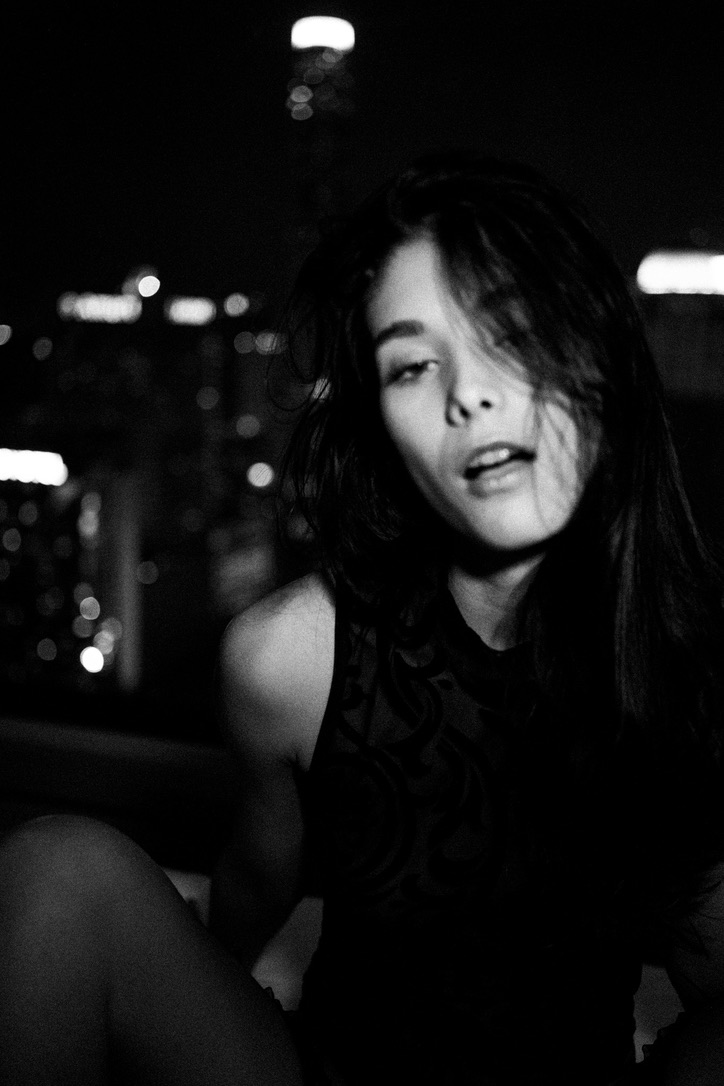 Black and white portrait of a woman with a city skyline in the background at night.